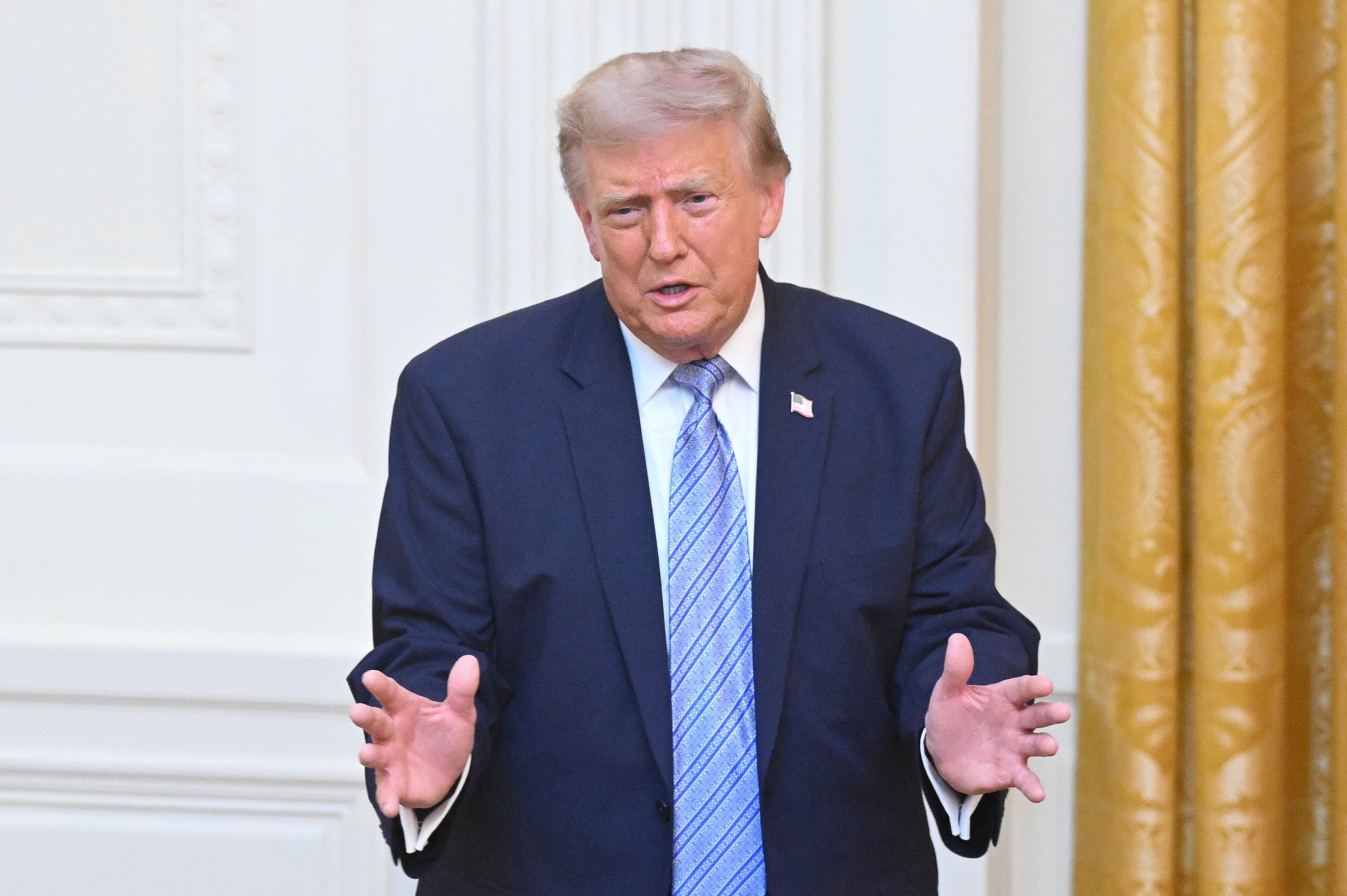 Donald Trump en traje oscuro hablando en un podio con micrófonos