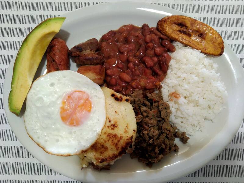 La bandeja paisa es uno de los platos más emblemáticos de Colombia, conocido por su abundante combinación de ingredientes como arroz, frijoles, carne de cerdo y huevo frito, que reflejan la riqueza y diversidad de la cocina colombiana. (Fuente: PapiPijuan en Wikimedia Commons)