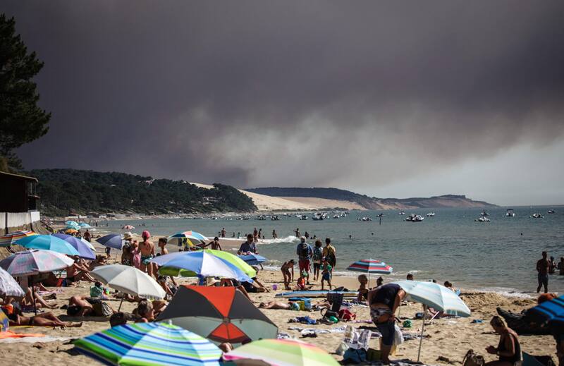 Turistas en la playa de "Pyla sur Mer", mientras una nube de humo negro se eleva al fondo por un incendio que en el bosque de La Teste-de-Buch. Según el Ministro del Interior francés, 2800 hectáreas de pinos fueron dañadas