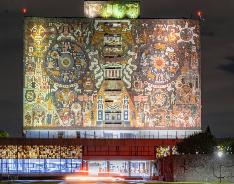 La emblemática fachada de la UNAM iluminada en la noche. Foto: Pexels.