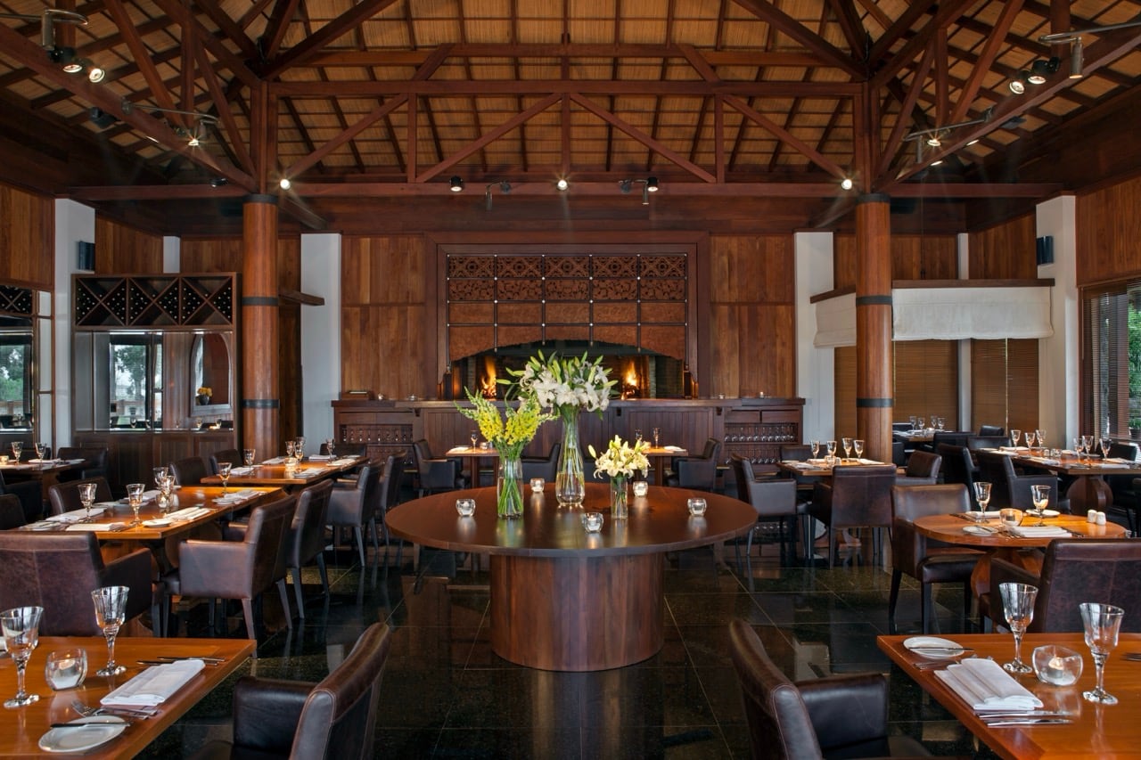Restaurante Pura: comedor con techos de madera a la vista, mesa con flores frescas y ambiente cálido.