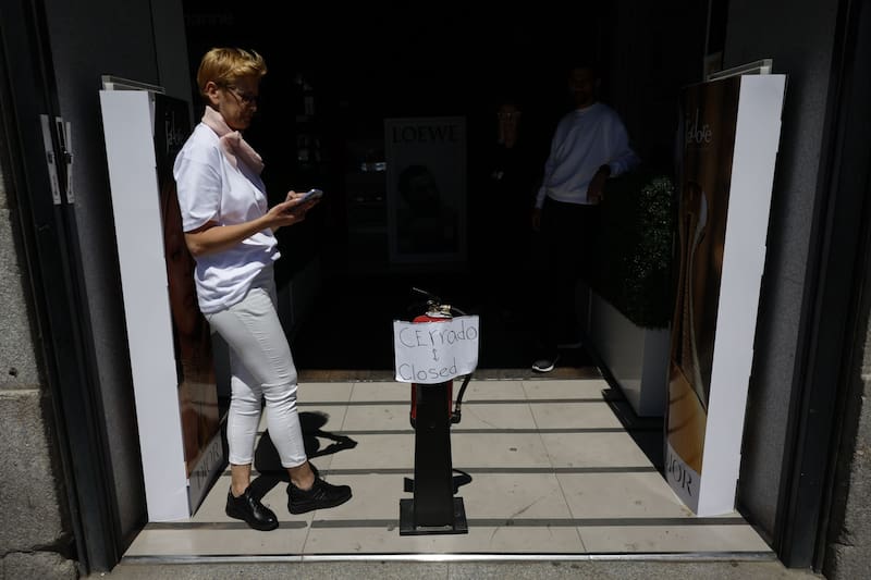 Una mujer revisa su móvil ante una tienda cerrada debido al apagón en un comercio del centro de Madrid, tras el corte de suministro eléctrico que afecta este lunes a España. (Fuente: EFE / Mariscal)