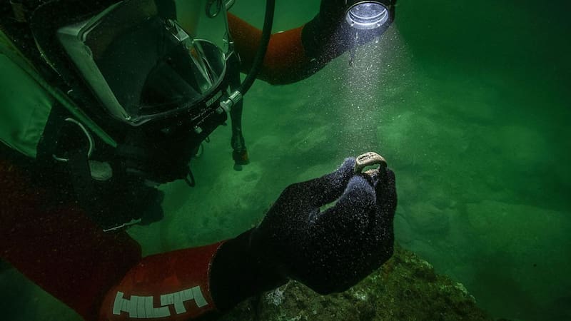 Un buzo de la misión arqueológica inspecciona con linterna el anillo de bronce hallado bajo el agua.