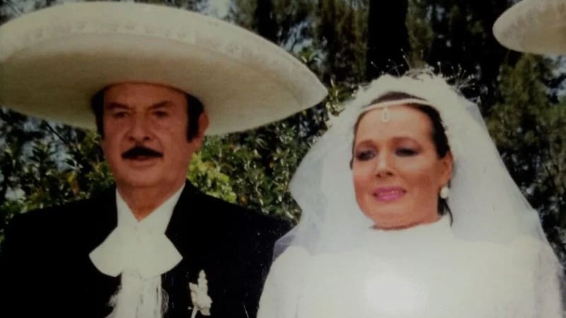 Retrato del matrimonio entre Antonio Aguilar, vestido con traje de charro y sombrero blanco, y Flor Silvestre lucida en su vestido de novia con velo.