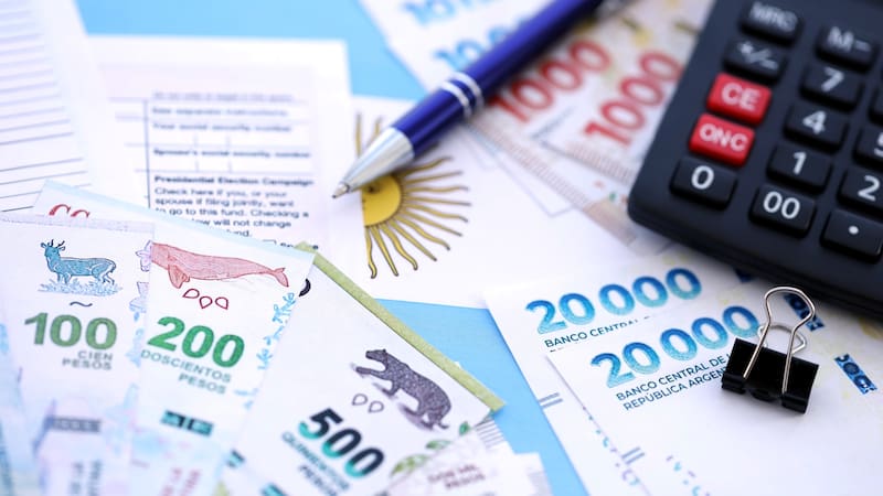 Argentine pesos money bills in big amount lies on table with pen, calculator, passport and tax forms