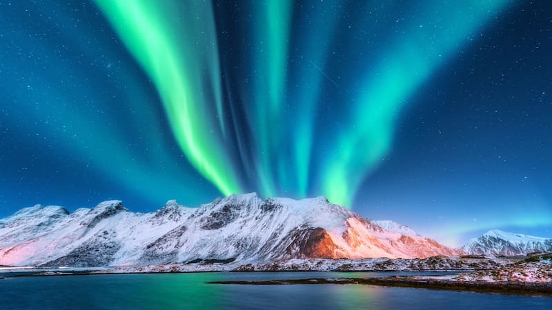 Aurora borealis. Lofoten islands, Norway. Aurora. Green northern lights. Starry sky with polar lights. Night winter landscape with aurora, sea with sky reflection and snowy mountains.Nature background