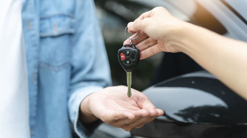 Una persona entregándole las llaves del auto a otra.