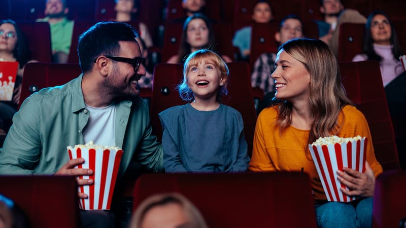 A young Caucasian family is spending their weekend hanging out together at the movie theater watching an entertaining movie together.