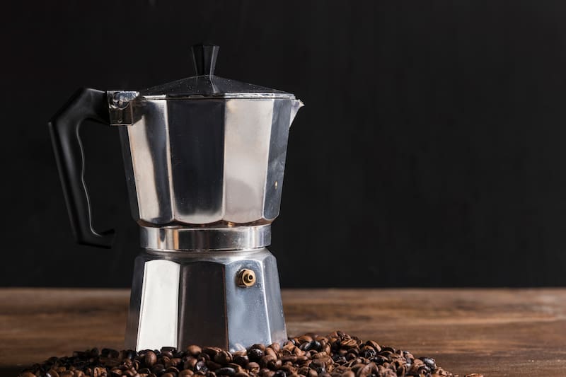 Cafetera italiana moka con granos alrededor en fondo de madera