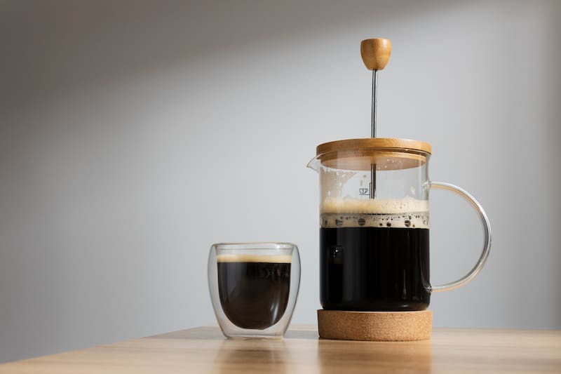 Cafetera prensa francesa con café hecho y una taza de café al lado