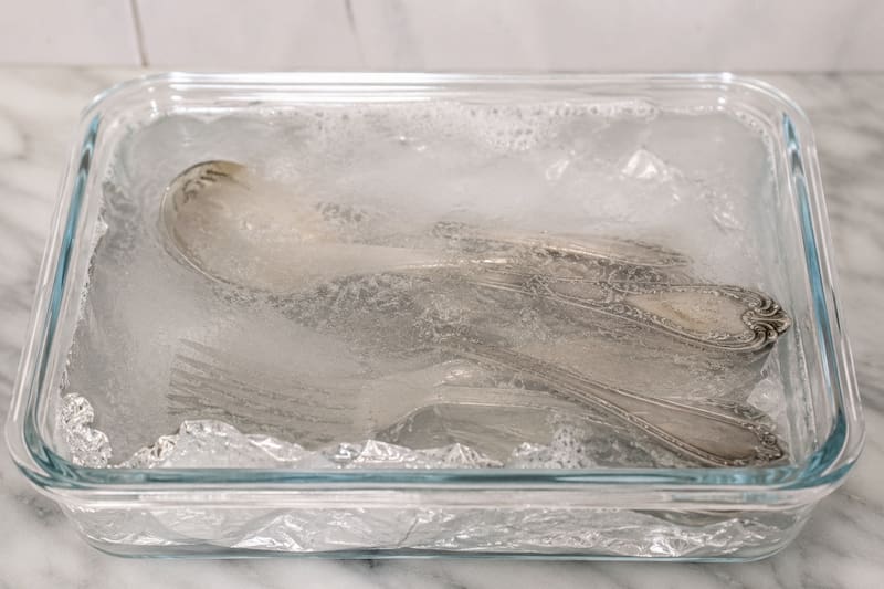 Colocar una hoja de papel aluminio en el fondo de un recipiente con agua caliente y bicarbonato de sodio, y sumergir las piezas de plata.