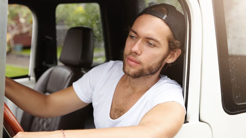 Un joven conductor al volante de un vehículo observa atentamente por la ventana mientras maneja.