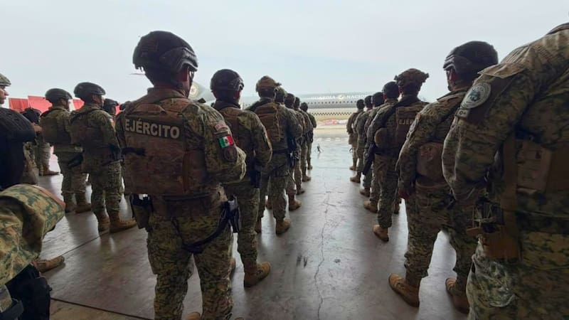 Elementos del Ejército Mexicano equipados con uniforme táctico y casco permanecen formados en filas dentro de un hangar frente a una aeronave de la Guardia Nacional.