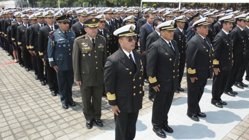 Mandos y oficiales de las Fuerzas Armadas alineados en posición de firmes portando sus trajes y gorras de gala durante una ceremonia oficial al aire libre.