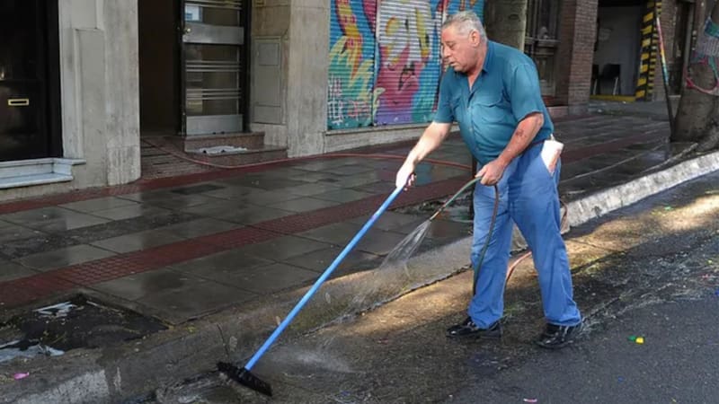 Encargado de edificio echando agua sobre la vereda.