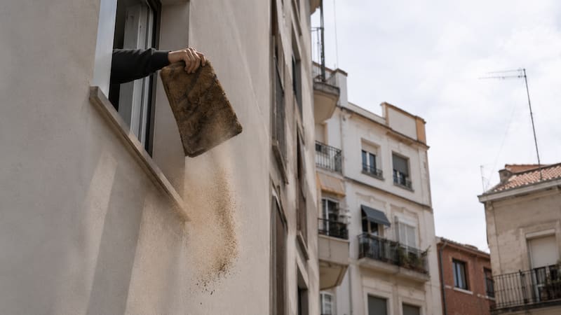 Es oficial | Los ayuntamientos podrán multar con hasta 3000 euros a los vecinos que sacudan el felpudo por la ventana. Fuente: imagen ilustrativa creada con ChatGPT.