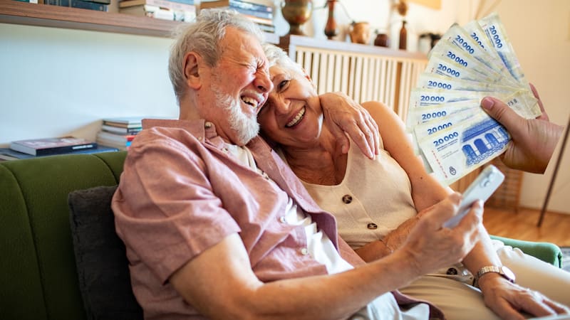 Happy senior couple using smartphone together on couch at home