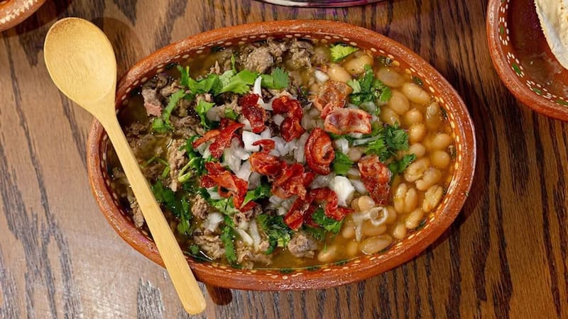 Cazuela artesanal de barro servida la tradicional carne en sus jugos, acompañado de frijoles de la olla, tocino crujiente, cebolla y cilantro picado.