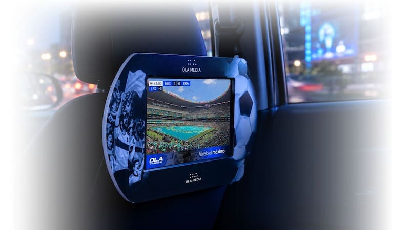 Vista en detalle de una pantalla interactiva de OLA Media instalada en el reposacabezas de un auto, transmitiendo un partido de fútbol entre México y Brasil con la marca OLA STADIUM.