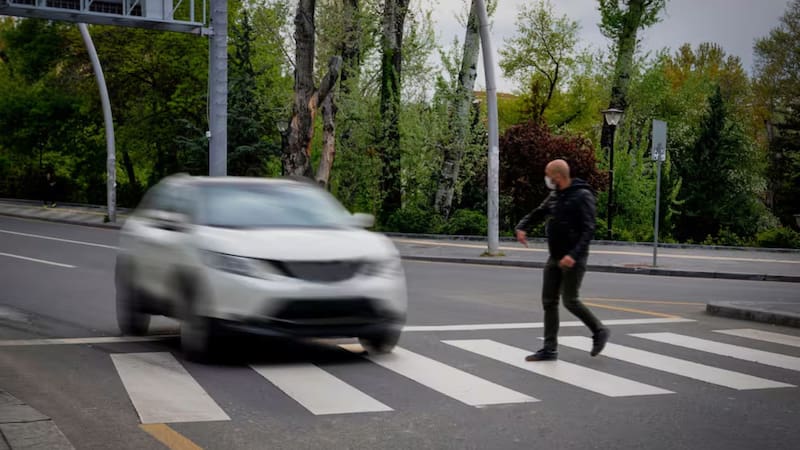 Un peatón cruza por el paso cebra mientras un automóvil transita a su lado en una vía urbana.