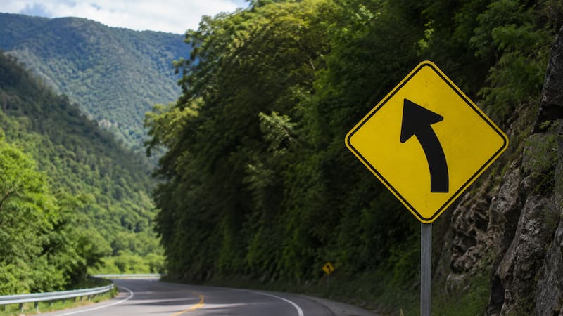 Qué significa la señal de tránsito con una flecha con curva en diagonal en fondo amarillo y bordes negros.
