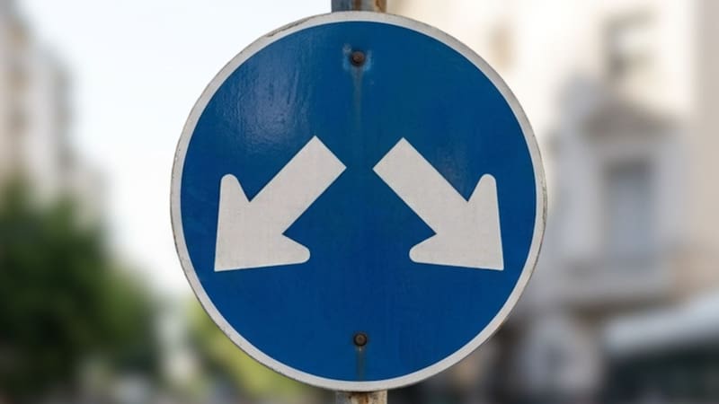 Qué significa la señal de tránsito azul con dos flechas blancas hacia abajo y en distintas direcciones.