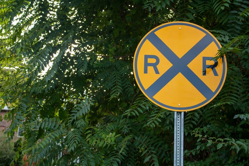 El cartel redondo, de fondo amarillo y con una "X" negra junto a dos "R" indica que hay vías de tren más adelante.
