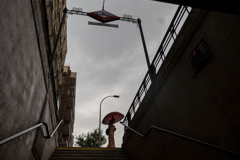 MADRID, 25/06/2026.- Una mujer con paraguas junto a la boca de Metro de Iglesia, en Madrid. La Agencia Estatal de Meteorología (Aemet) da por finalizada el jueves la primera ola de calor que se ha registrado en España este verano, con un descenso de temperaturas generalizado gracias a la entrada de una masa de aire atlántica más fría por el oeste, aunque todavía habrá valores altos en el nordeste y Baleares. EFE/DAniel Gonzalez