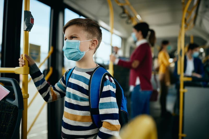 Pensive boy wearing face mask while commuting to school by bus during coronavirus pandemic.