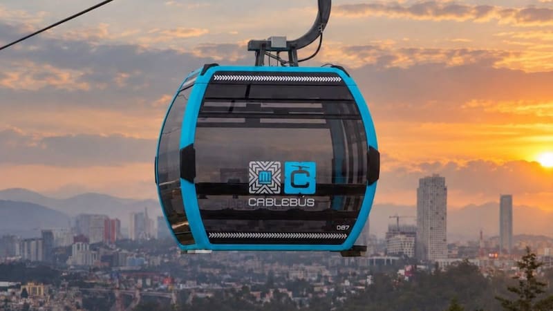 Cabina de Cablebús en funcionamiento durante el atardecer con la panorámica urbana de fondo.