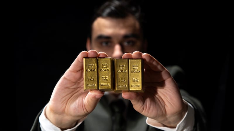 Young man investing in gold, holding gold bars, gold holdings concept. Savings and investments, business and finance